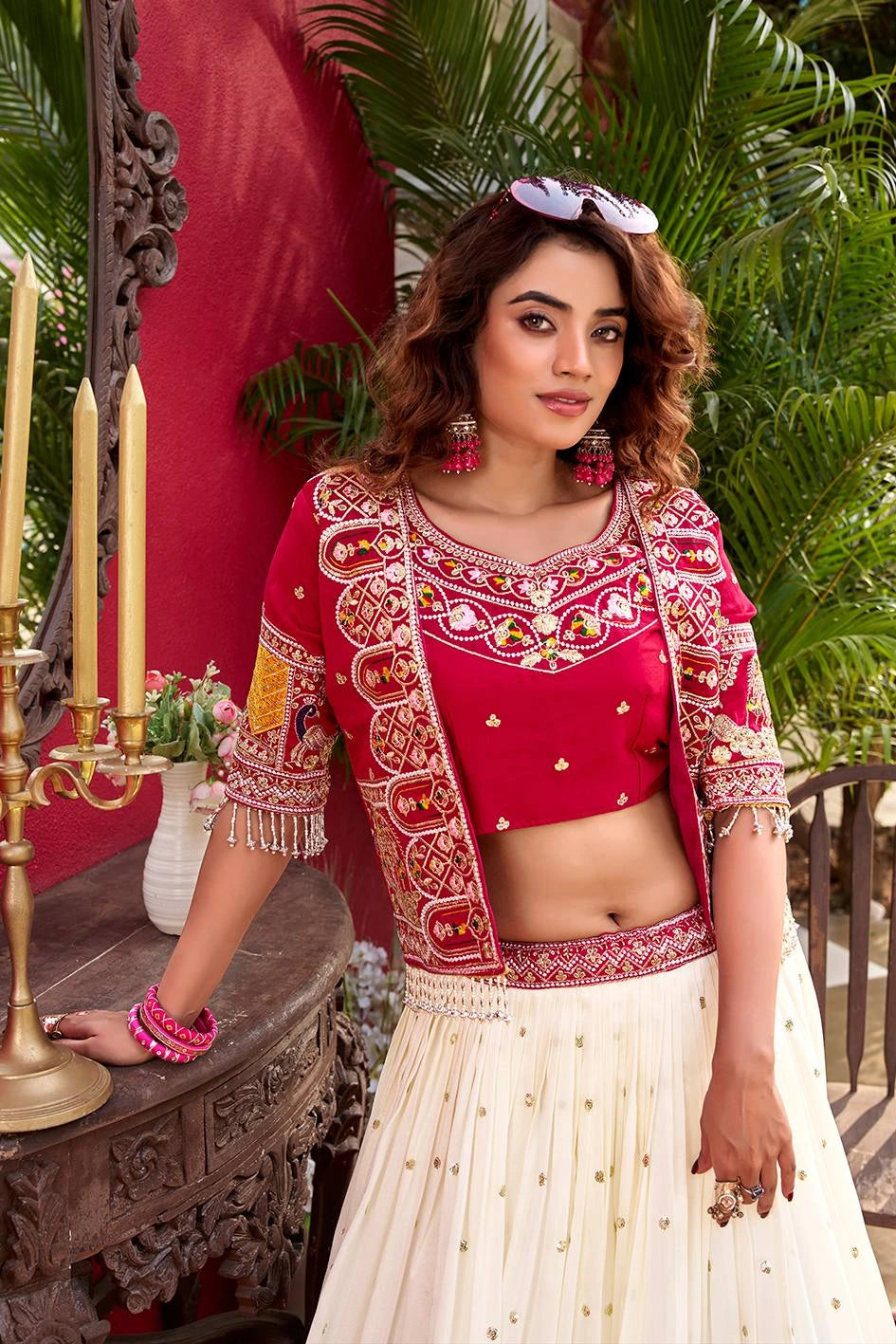 Woman in a red and white traditional outfit standing in a decorated room with candles and plants.